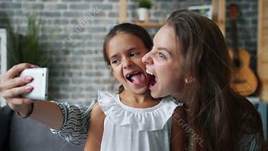 Playful mother taking selfie with adorable little daughter having fun in house