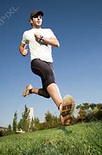 Determined Young Man Running and Jogging in a Sunny Park with Blue Sky Background