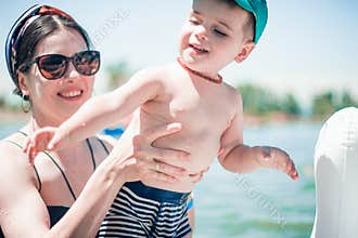 A cute little boy in a blue baseball hat and young attractive mom in sea with an inflatable ring