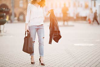 Brunette woman in hat walking at sunset after shopping.