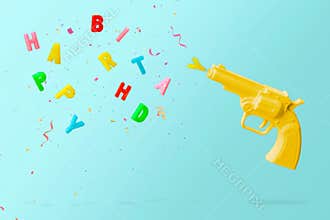 Yellow pistol shooting colorful birthday candles and colorful confetti, against  blue background. Happy birthday  concept with