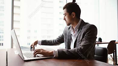 Serious young man neurologist doctor working typing on laptop computer, looking at MRI scan of head