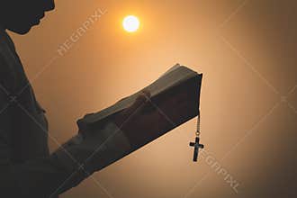 A woman studying the scriptures and having a cross. Sunrise or sunset background, open study concept of the christian scriptures