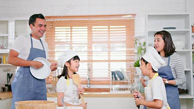 Young Asian family of mother, father, daughter and son enjoy play, sing, dance together in home kitchen