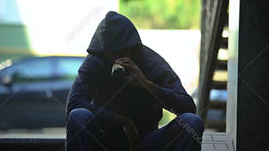 Troubled teenager drinking beer sitting on steps in gateway, lost in life