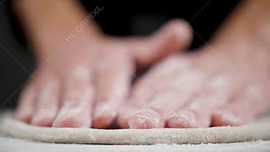 Cook prepares wheat dough for pizza on the black background