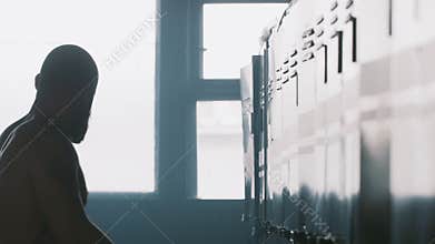 Silhouette of young male athlete alone in dark gym changing room hitting locker, overcoming failure stress and pressure.