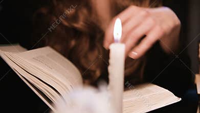 Closeup attractive caucasian girl leafing through a book. Candles are burning. Halloween celebration concept. Shallow