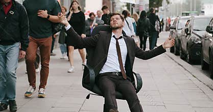 fired employee rides on office chair among people in street throwing documents