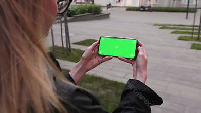 Point of View of woman holds horizontal mobile phone two hand outdoor urban city. Use green screen for copy space