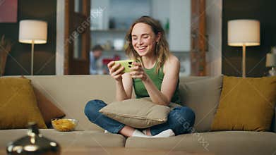 Excited woman laughing smartphone at home couch. Happy lady playing mobile phone