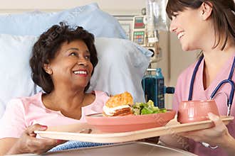 Nurse Serving Senior Female Patient Meal In Hospital Bed