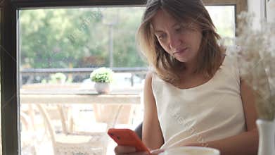 A woman with a phone in her hand sits at the window of a coffee shop