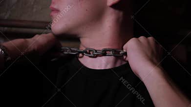 Close-up of a young guy chained by the neck in a creepy dark room. Quest.