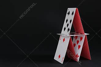 House of playing cards on black background, space for text