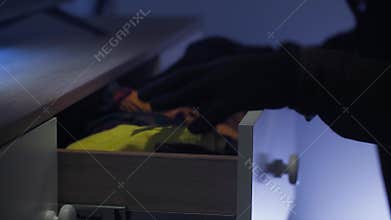 a robber in a balaclava and black clothes entered someone else's apartment and opened drawers in a chest of drawers