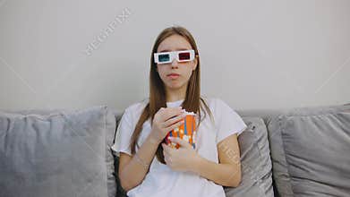 A young woman wearing stylish 3D glasses is fully immersed in a delightful movie experience from the comfort of her own