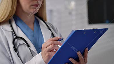 Female Doctor Writing on Blue Clipboard in Hospital Setting