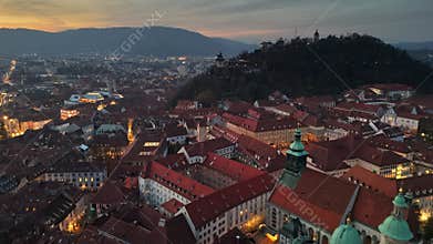 Aerial sunset view over Graz, Austria showcasing historic rooftops and vibrant city lights. Flying over Graz old town in