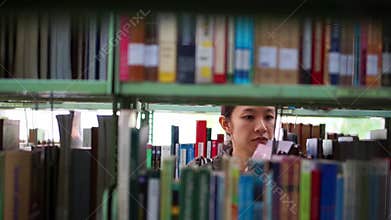 Girl student walking between shelves, searching for books
