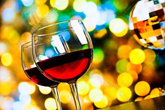 Two red wine glasses against colorful bokeh lights and sparkling disco ball background