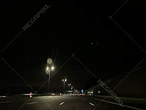Night highway view with glowing streetlights, blurred traffic, lane markings, and