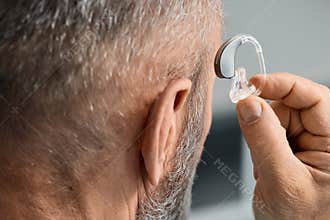A man tries on his custom-made behind-the-ear hearing aid by putting it on his own ear. Hearing solutions for hard of hearing