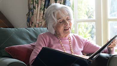 Senior Woman In Armchair At Home Looking At Photo Album