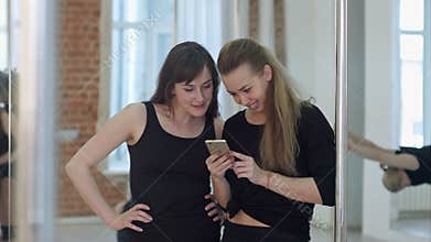 Cute happy pole dancers taking a break from their workout and social networking with a cell phone
