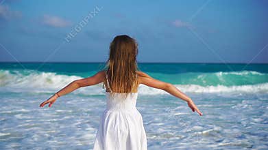 Adorable happy little girl on white beach looking on the ocean. Noisy sea and a small cute kid