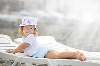 Child laying on the beach chaise long in the sun light