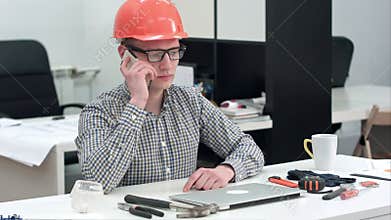 Young architect in helmet having important phone call
