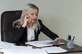Beautiful smiling business woman working at her office desk with documents and talking on the phone.