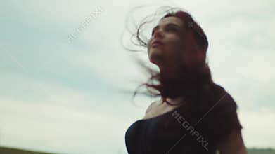 Gorgeous young woman in a black bare shoulder dress walking through the field of golden wheat, stroking her hair