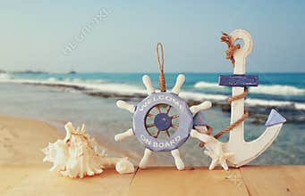 Old nautical wood wheel, anchor and shells on wooden table over sea background.