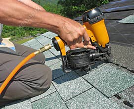 Carpenter uses nail gun to attach asphalt shingles