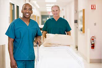 Two Orderlies Pushing Bed Down A Hospital Corridor
