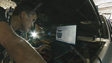 Car service, computer diagnostics: mechanic repairs the damage using the pc in car service