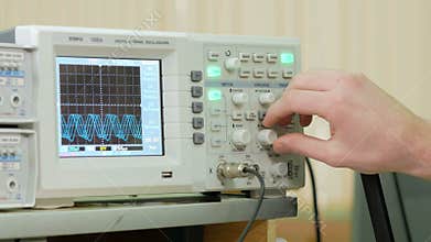 Men`s engineering arm adjusts the oscilloscope for proper display of the electrical signal. Modern small industrial