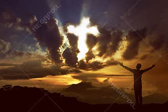 Man praying to god with ray of light shaping cross on the sky