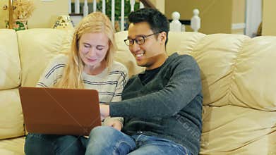 Multinational couple relaxing at home, sitting on couch, laptop use