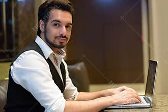 Young handsome Indian man using laptop in the lobby of hotel