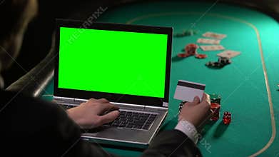 Man paying poker bet with credit card, using laptop green screen, online winning