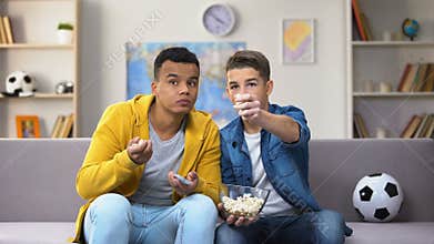 Anxious teenage friends watching football match on TV and eating popcorn leisure