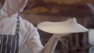 Young guy spinning and tossing two disks of pizza dough in kitchen in a restaurant. Professional pizzaiolo making pizza
