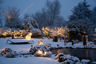 Snow in illuminated garden on winter evening. Beautiful illuminated private garden with illumined glass light objects