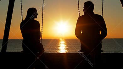 Couple swinging looking each other at sunrise