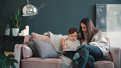 Beautiful young mother sitting on the sofa in your house the living room reads son a story in the ear and learn to read