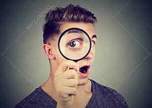 Curious young man looking through a magnifying glass