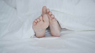 Crop female feet under blanket